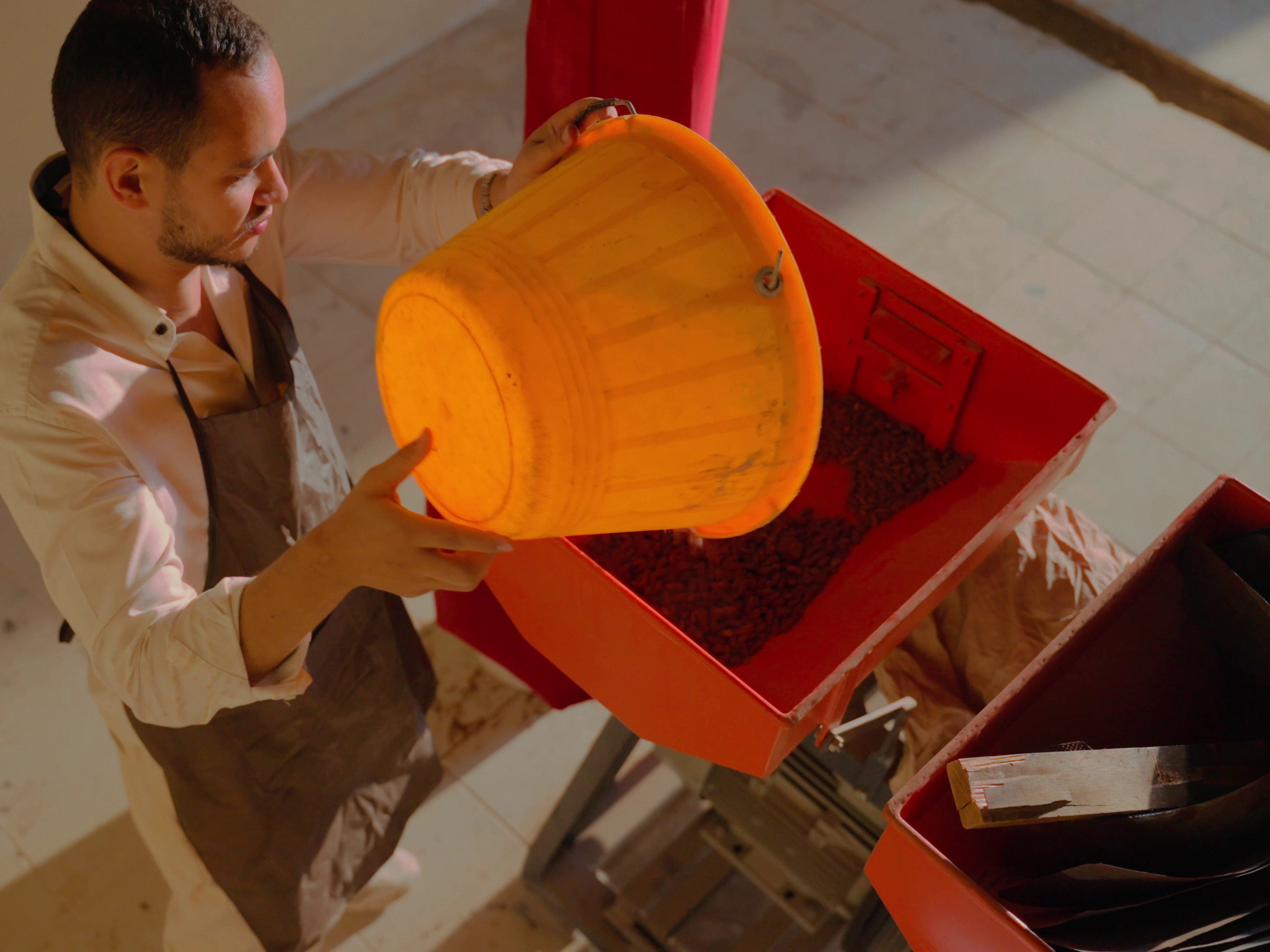 Khaled emptying a bucket of date seeds into a grinding machine.