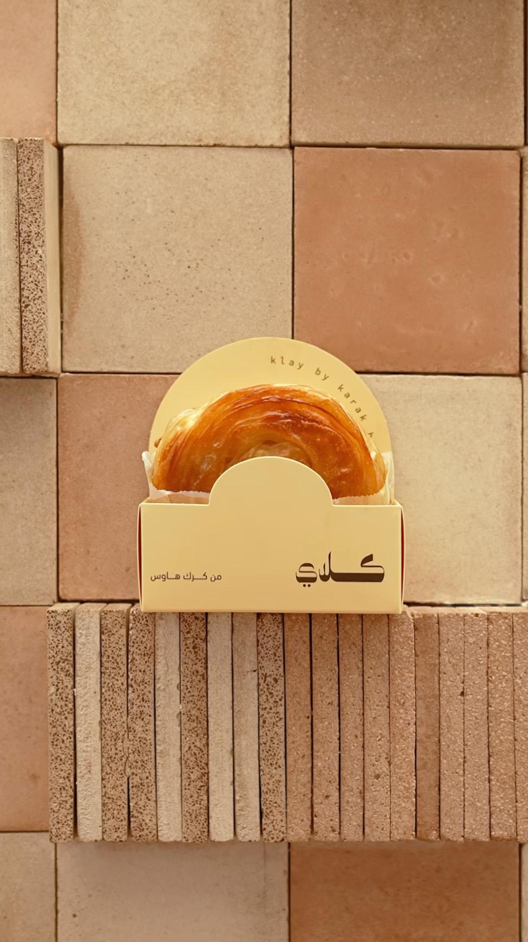 Close up of a pastry item in Klay's packaging, photographed against - and resting on - the Datecrete tiles on the shopfront's wall.