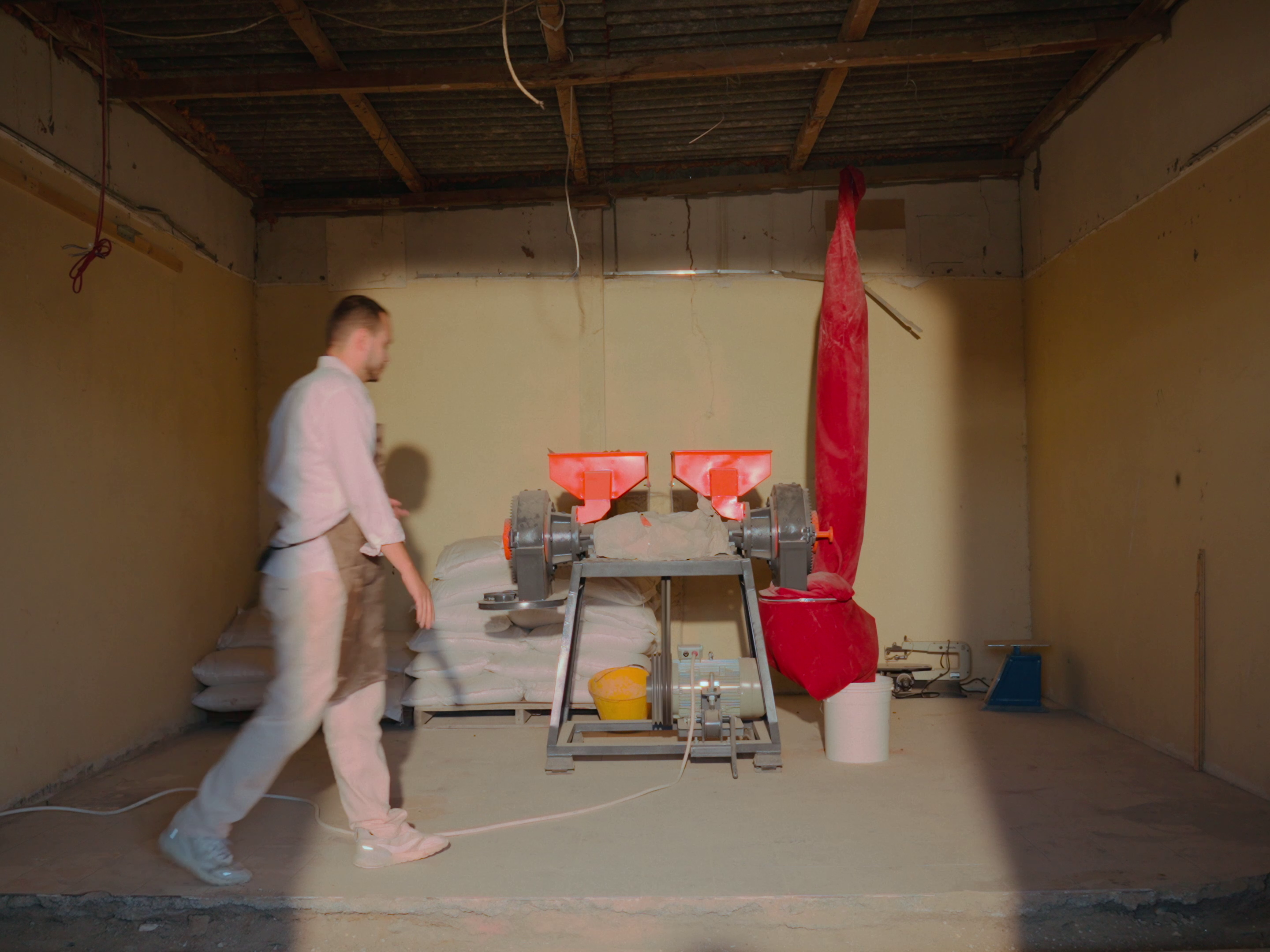 Far away shot of the entire grinding machine, with Khaled walking towards it.