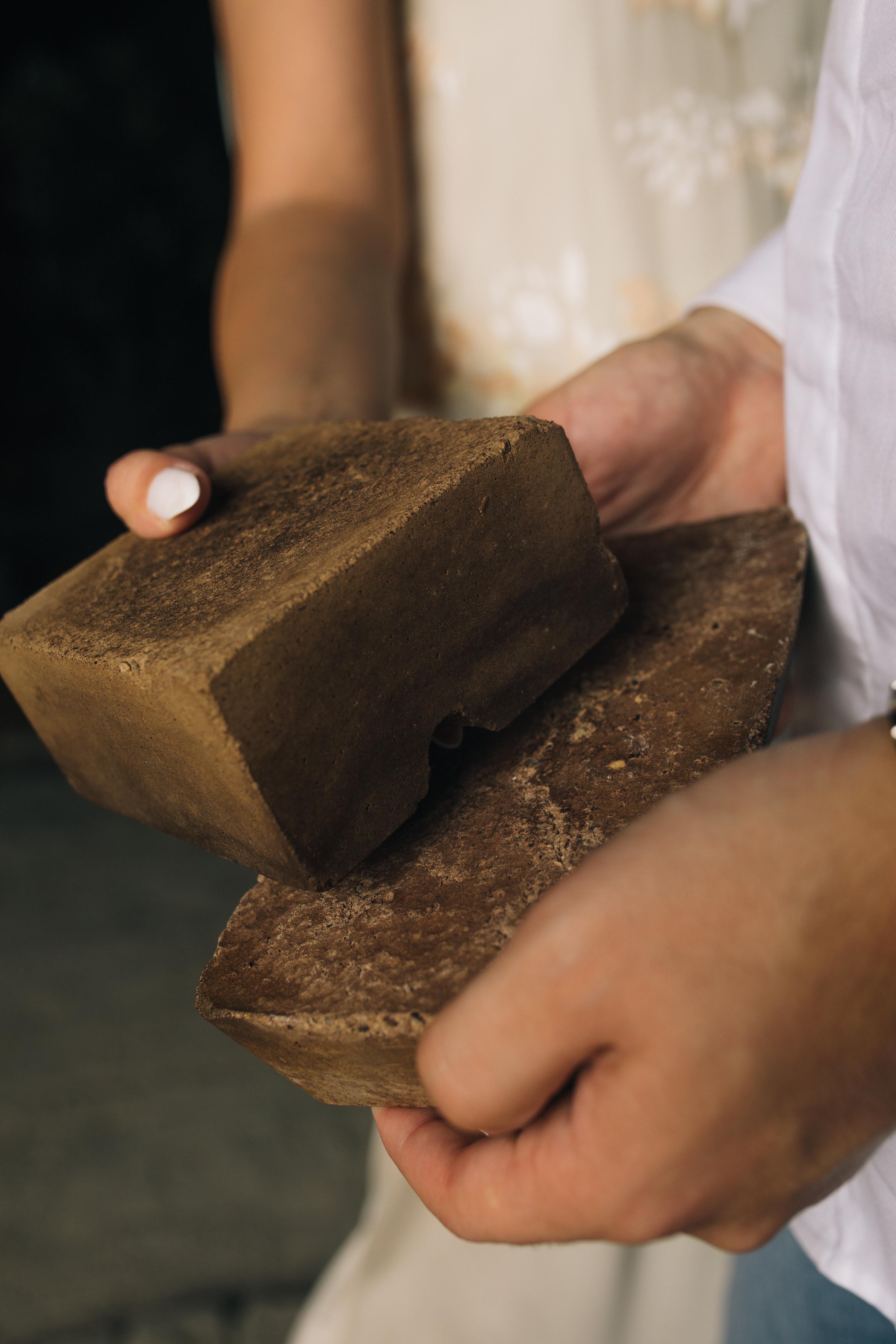 Sara and Khaled's hands, together, holding up a pair of prototype Datecrete bricks.